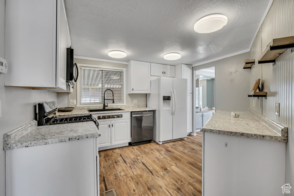 Kitchen featuring appliances with stainless steel finishes, light wood-style flooring, white cabinets, a textured ceiling, and crown molding