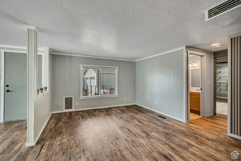 Unfurnished living room featuring wood finished floors, crown molding, and a textured ceiling