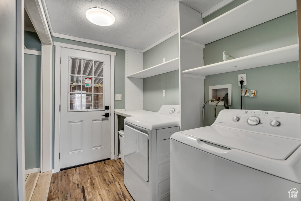 Laundry room with washer and clothes dryer, light wood-type flooring, and a textured ceiling