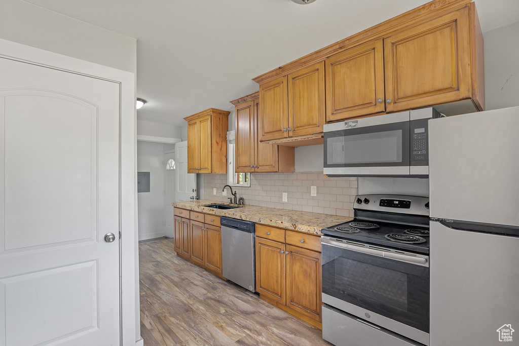 Kitchen featuring appliances with stainless steel finishes, light wood-type flooring, decorative backsplash, light stone countertops, and brown cabinets