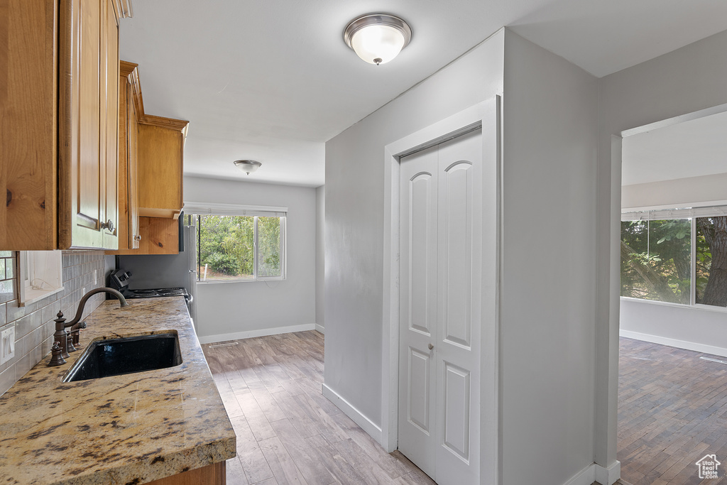 Kitchen featuring light wood-type flooring, backsplash, brown cabinets, and light stone countertops