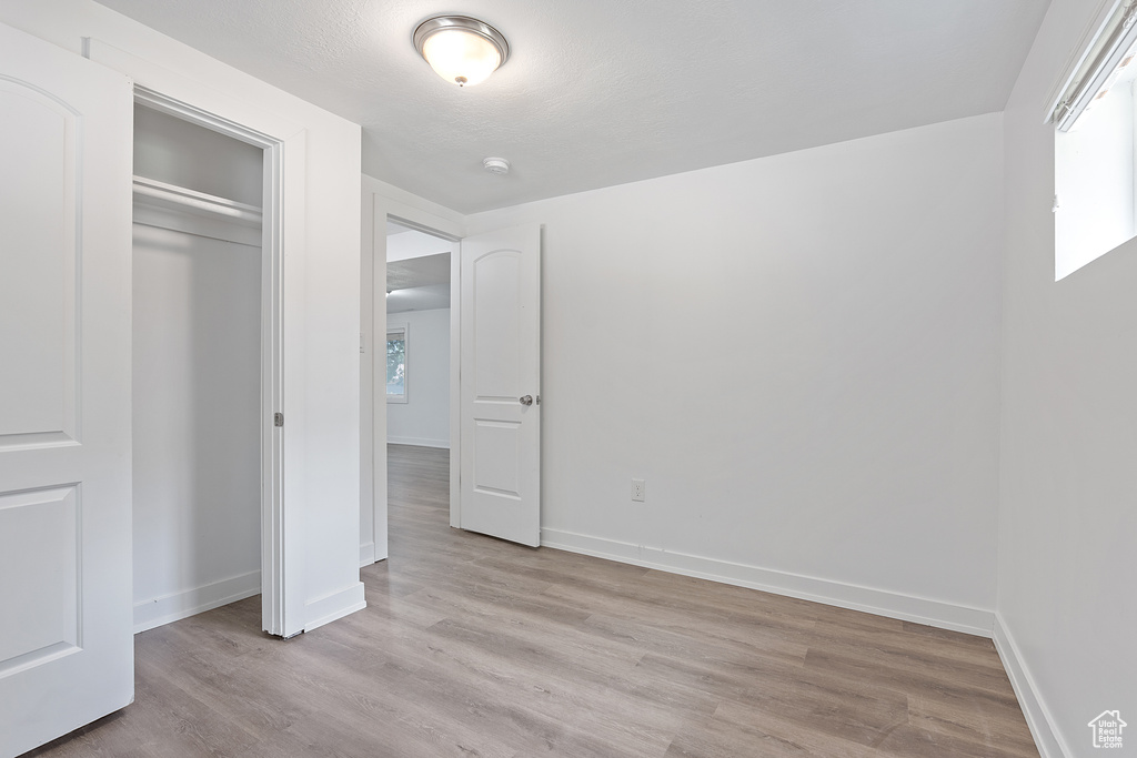 Unfurnished bedroom featuring light wood-type flooring, multiple windows, and a closet