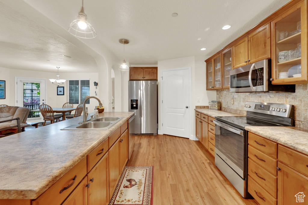 Kitchen with stainless steel appliances, light wood-style flooring, a chandelier, backsplash, and pendant lighting