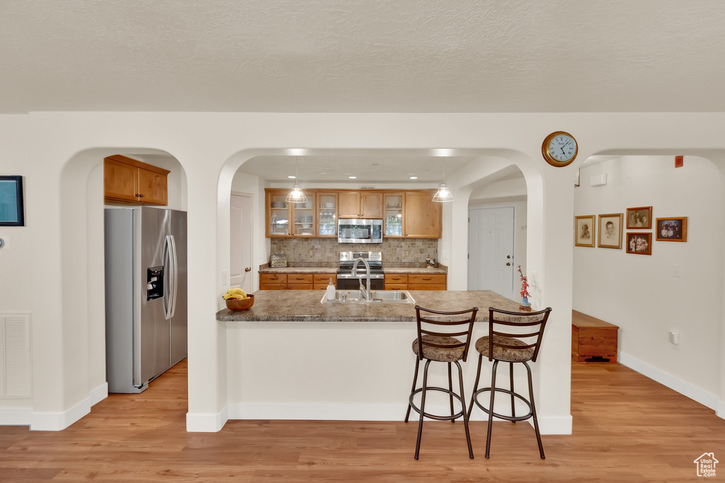 Kitchen with stainless steel appliances, light wood-style flooring, arched walkways, and brown cabinets