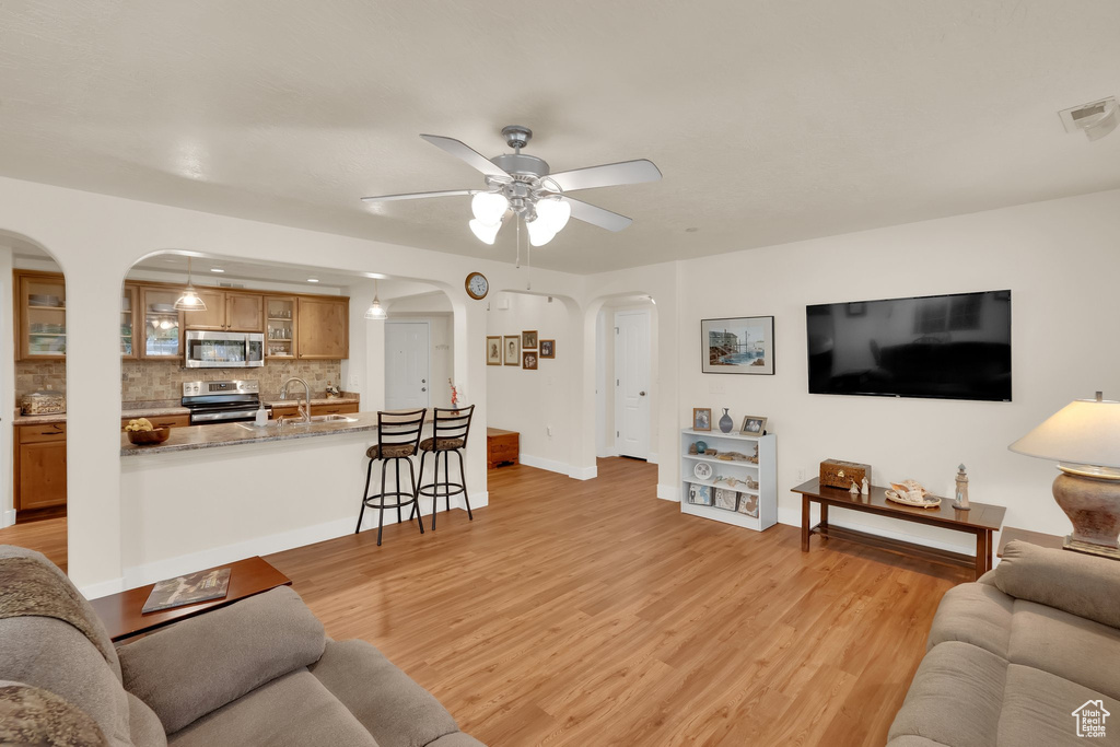 Living room with arched walkways, a ceiling fan, and light wood-style floors