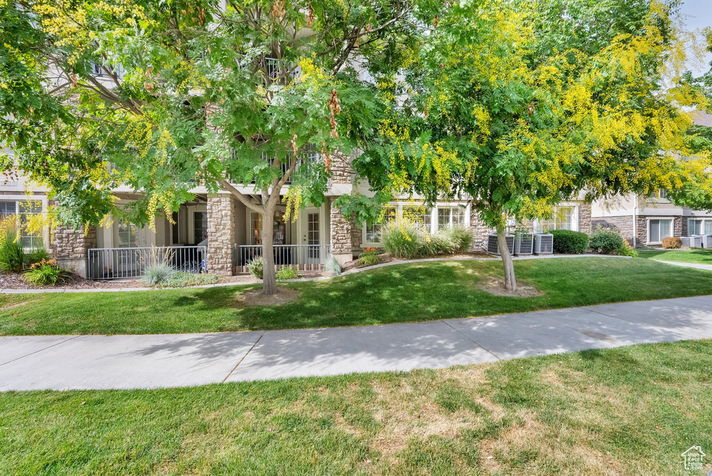 View of property hidden behind natural elements featuring stone siding and a front yard