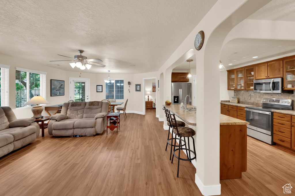 Living room featuring light wood-style floors, arched walkways, a textured ceiling, and a ceiling fan