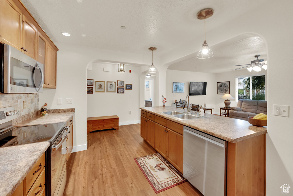 Kitchen featuring stainless steel appliances, arched walkways, light wood-type flooring, decorative light fixtures, and a ceiling fan