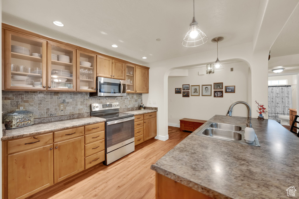 Kitchen featuring appliances with stainless steel finishes, arched walkways, backsplash, light wood-style flooring, and pendant lighting
