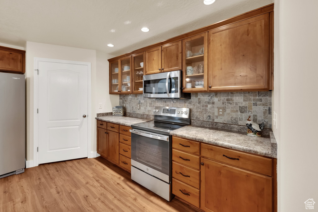 Kitchen featuring appliances with stainless steel finishes, brown cabinetry, light wood finished floors, tasteful backsplash, and recessed lighting