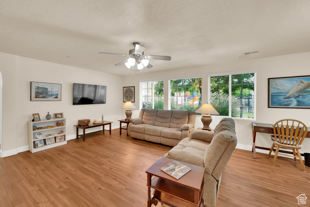 Living room featuring light wood-type flooring, a ceiling fan, and a textured ceiling