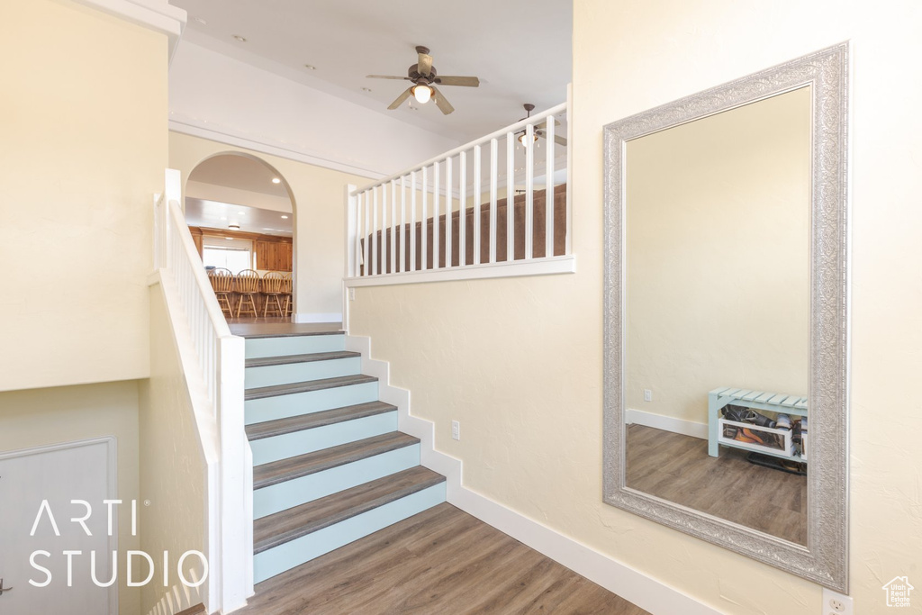 Staircase with a ceiling fan, wood finished floors, and arched walkways