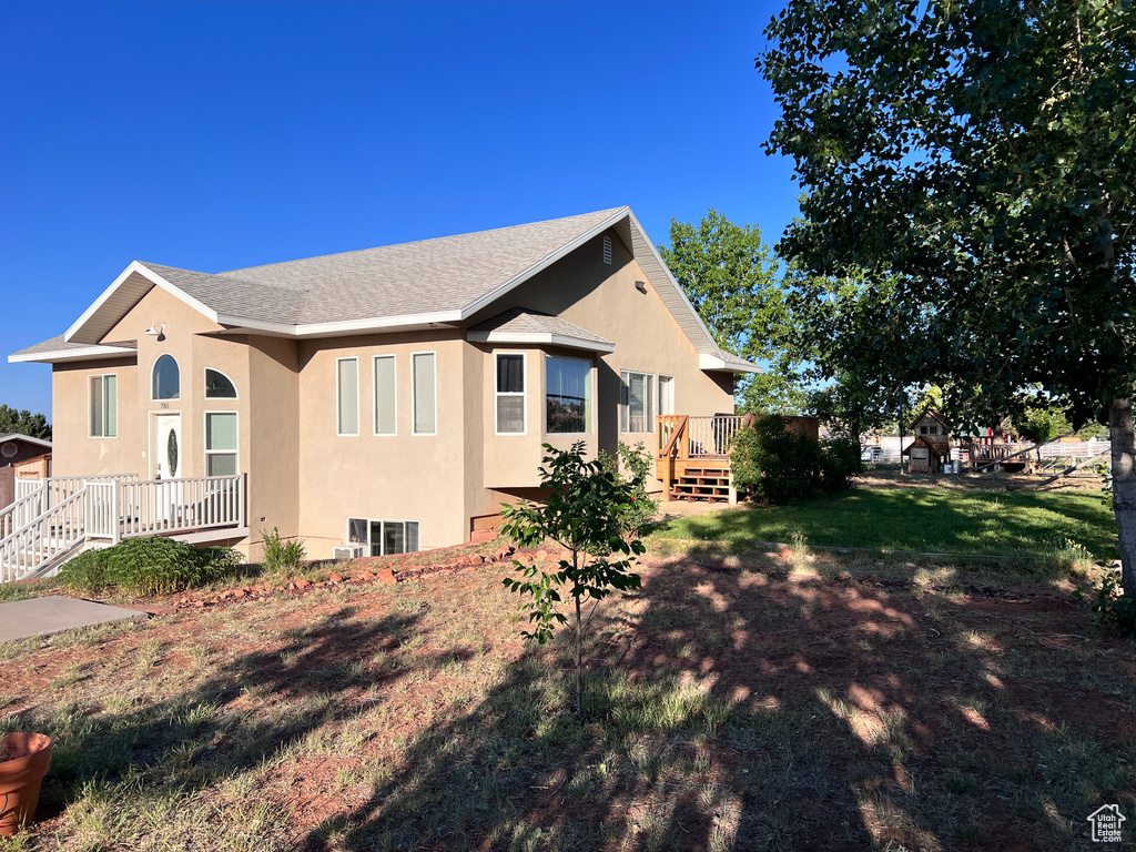 View of side of home with stucco siding, a wooden deck, roof with shingles, and a lawn