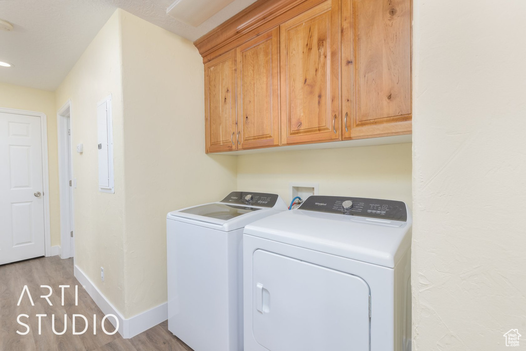 Laundry room featuring washing machine and clothes dryer, light wood finished floors, cabinet space, and electric panel
