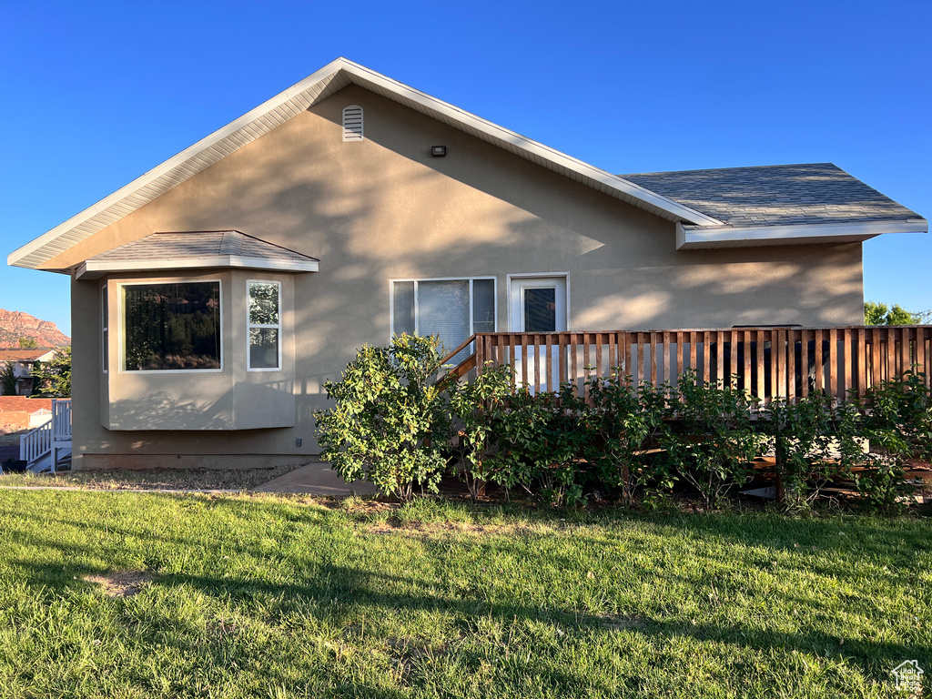 View of property exterior with a yard, stucco siding, and roof with shingles