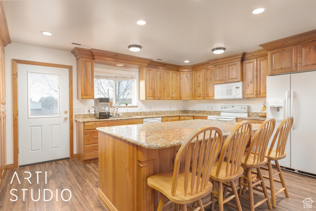 Kitchen featuring white appliances, a kitchen island, a kitchen breakfast bar, wood finished floors, and recessed lighting