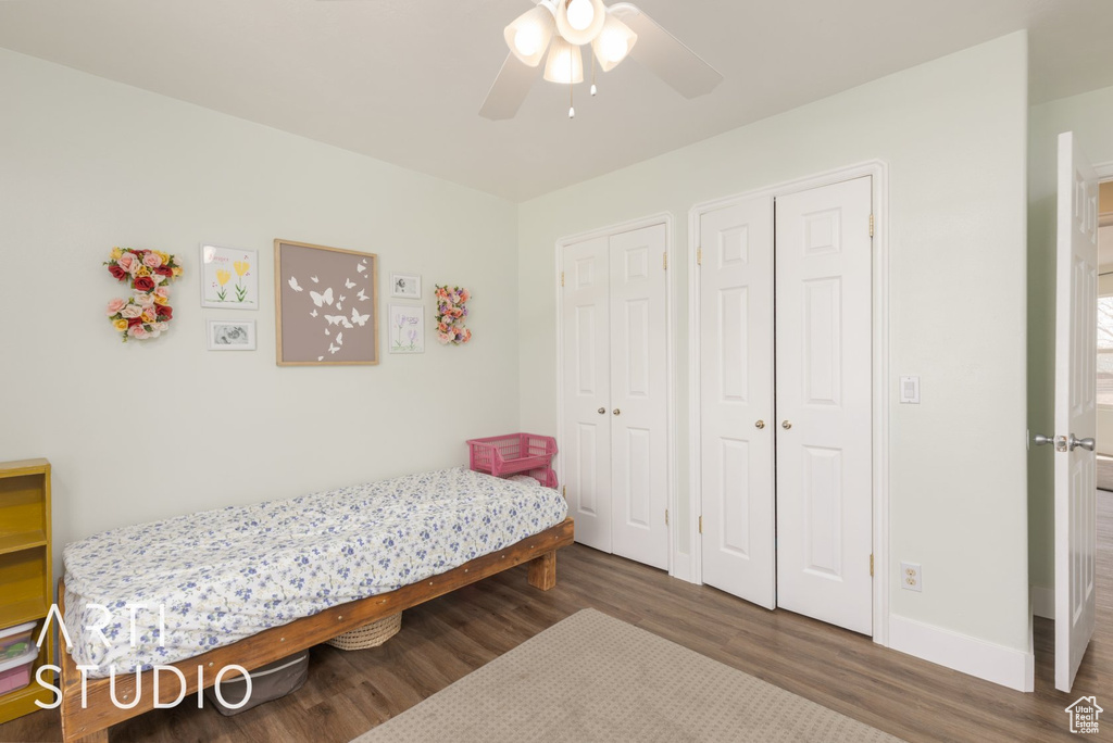 Bedroom with wood finished floors, two closets, and ceiling fan