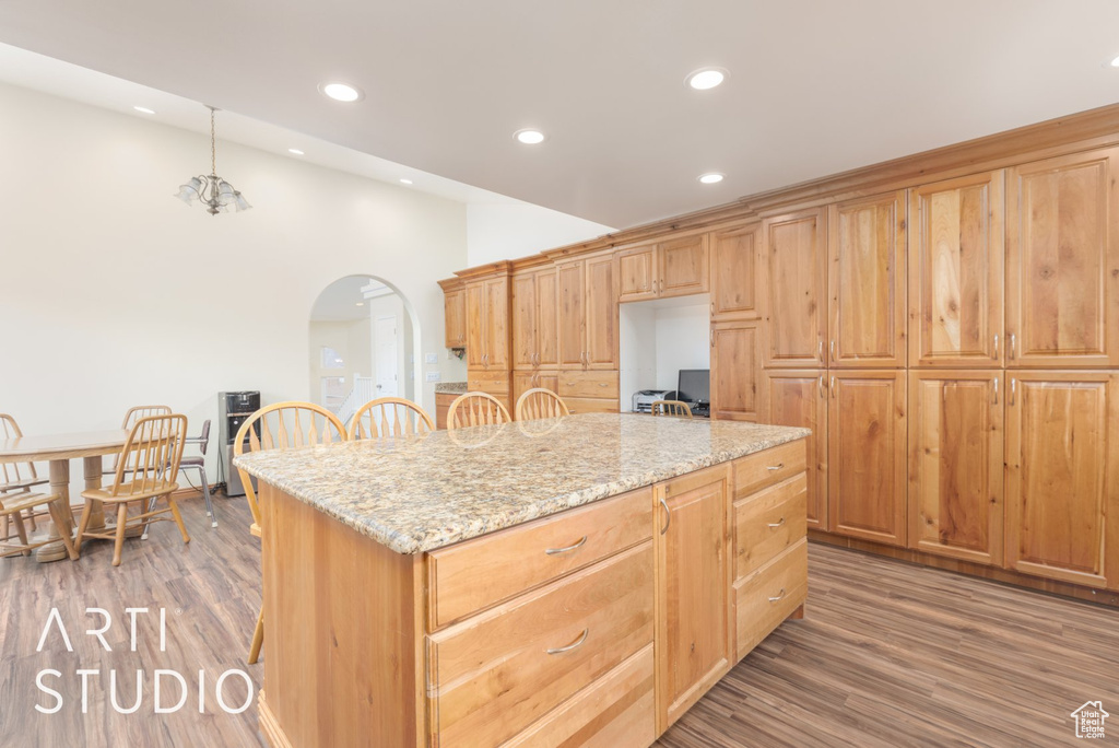 Kitchen featuring arched walkways, light wood-style floors, recessed lighting, a center island, and light stone countertops