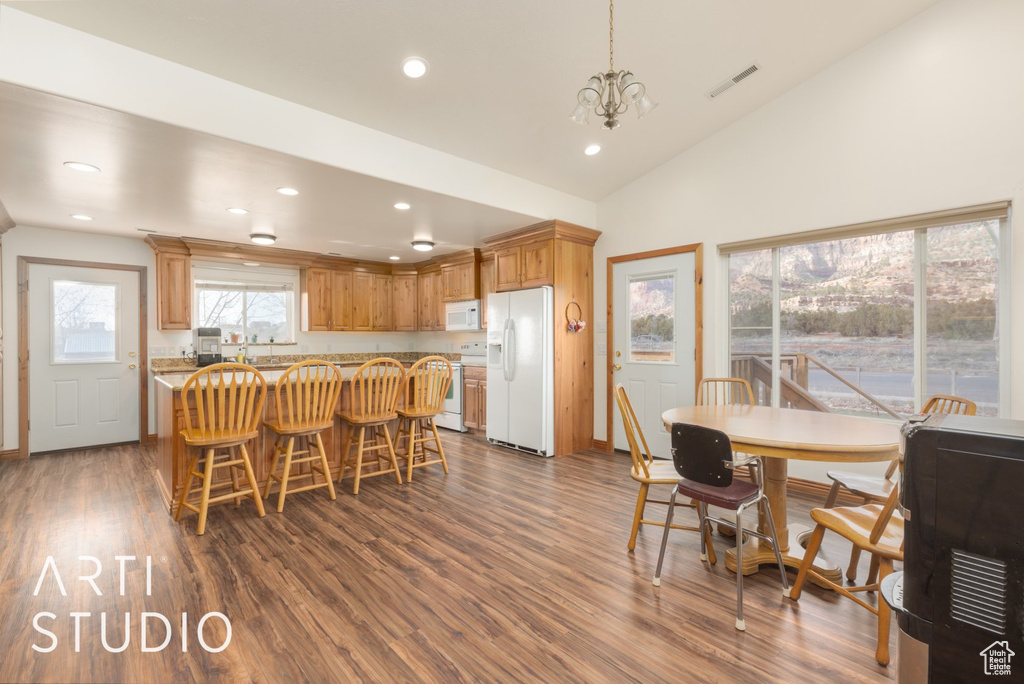 Kitchen featuring white appliances, dark wood-style flooring, recessed lighting, a kitchen bar, and a chandelier