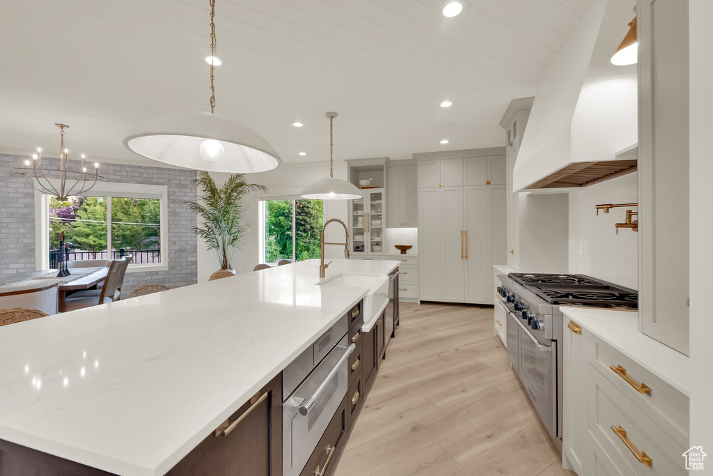 Kitchen with stainless steel range, a warming drawer, a spacious island, light wood finished floors, and custom range hood