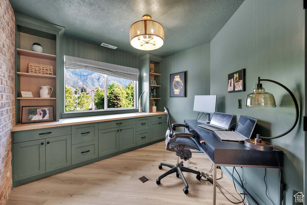 Home office with light wood-style floors, a textured ceiling, a chandelier, and brick wall
