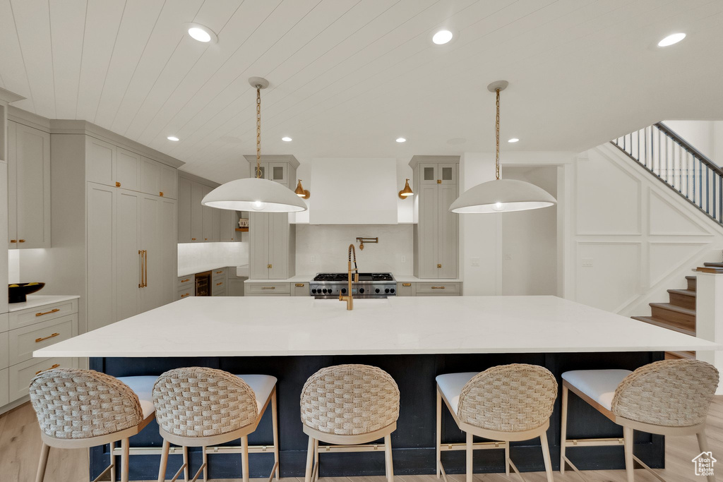 Kitchen featuring light countertops, a spacious island, a breakfast bar, glass insert cabinets, and recessed lighting