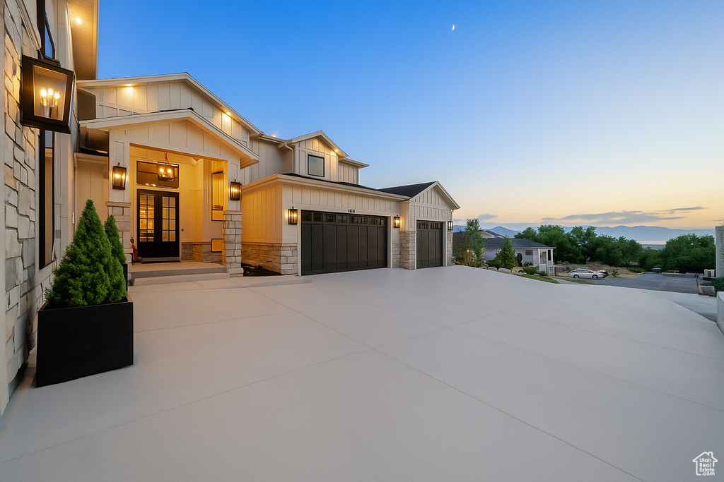View of front of house with board and batten siding, driveway, an attached garage, and stone siding