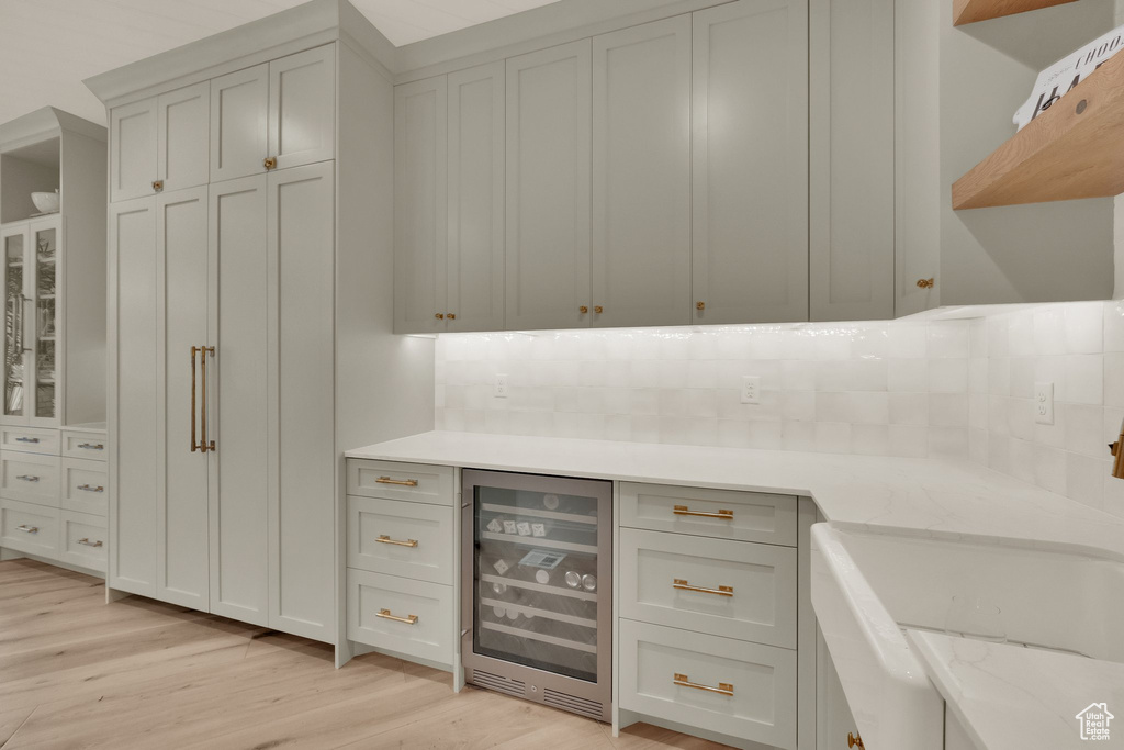Bar with beverage cooler, light wood-style floors, and backsplash