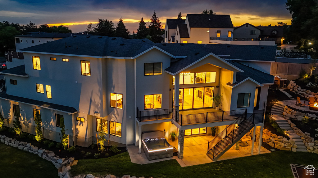 Back of house at dusk featuring stairway, stucco siding, a patio area, roof with shingles, and a lawn