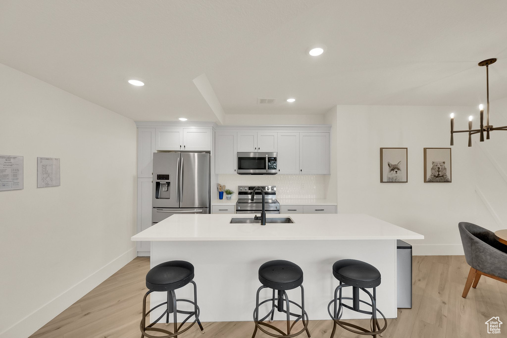 Kitchen with appliances with stainless steel finishes, a kitchen bar, light wood-style flooring, and recessed lighting