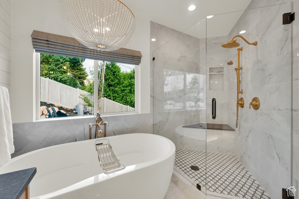 Bathroom featuring a freestanding bath, a marble finish shower, a chandelier, tile walls, and recessed lighting