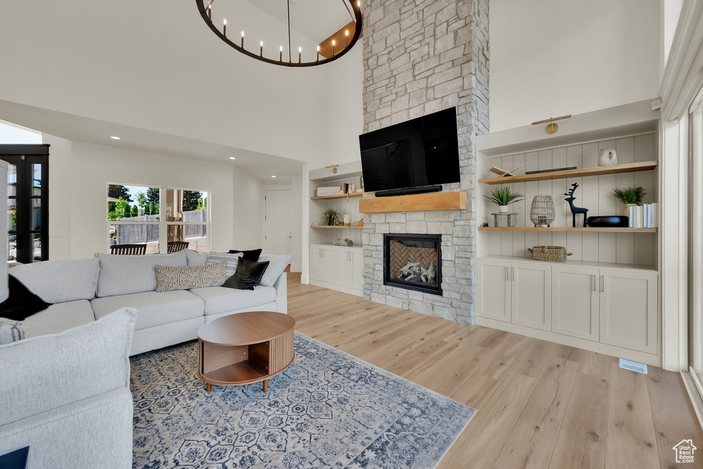 Living room featuring a stone fireplace, light wood-type flooring, a high ceiling, built in shelves, and a chandelier
