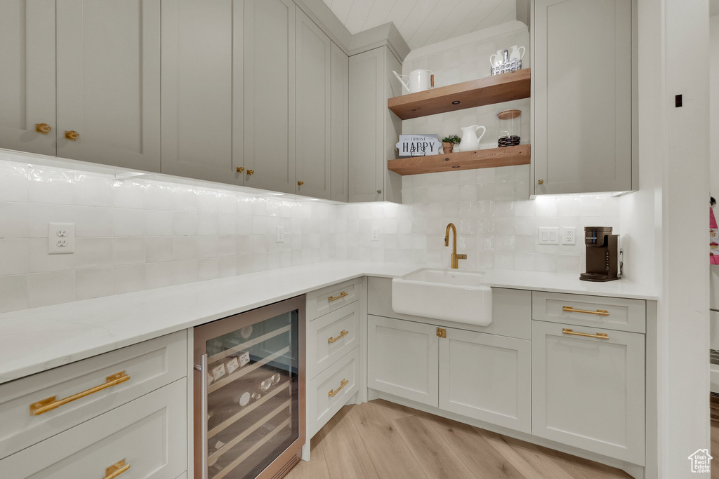 Bar featuring beverage cooler, tasteful backsplash, and light wood-style flooring