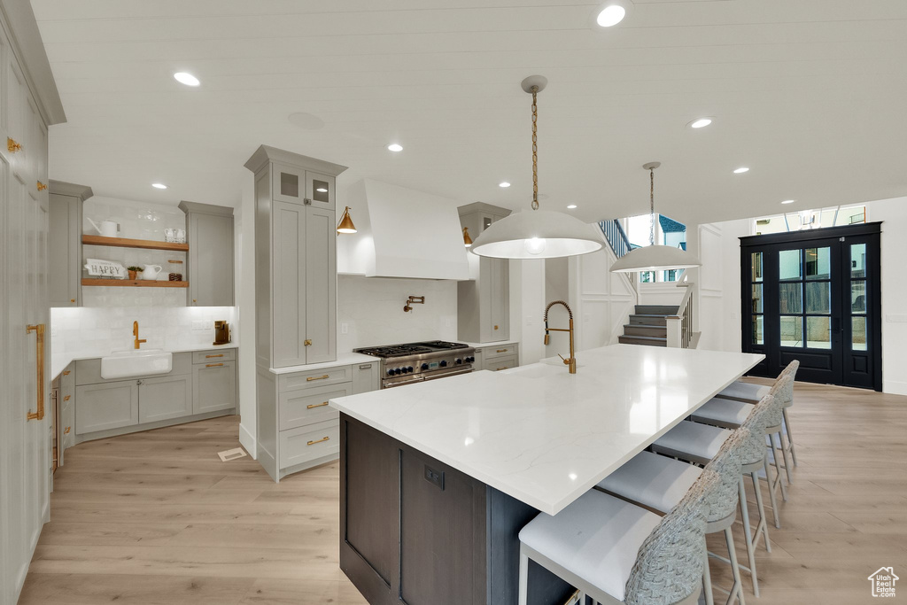 Kitchen featuring custom range hood, high end stainless steel range oven, tasteful backsplash, light wood finished floors, and recessed lighting