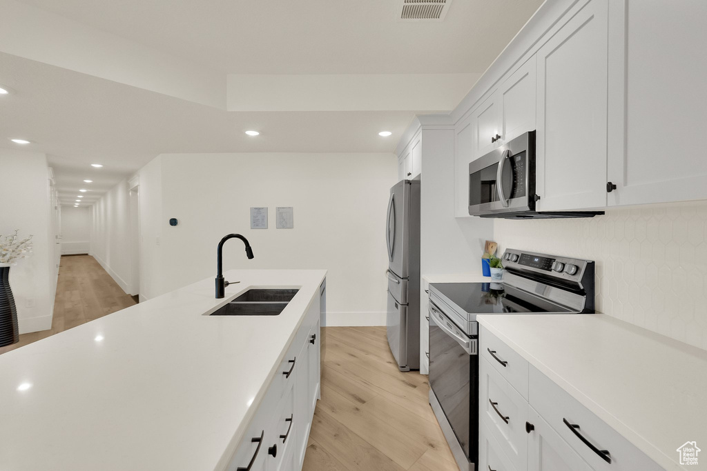 Kitchen featuring appliances with stainless steel finishes, recessed lighting, light wood finished floors, light countertops, and white cabinets