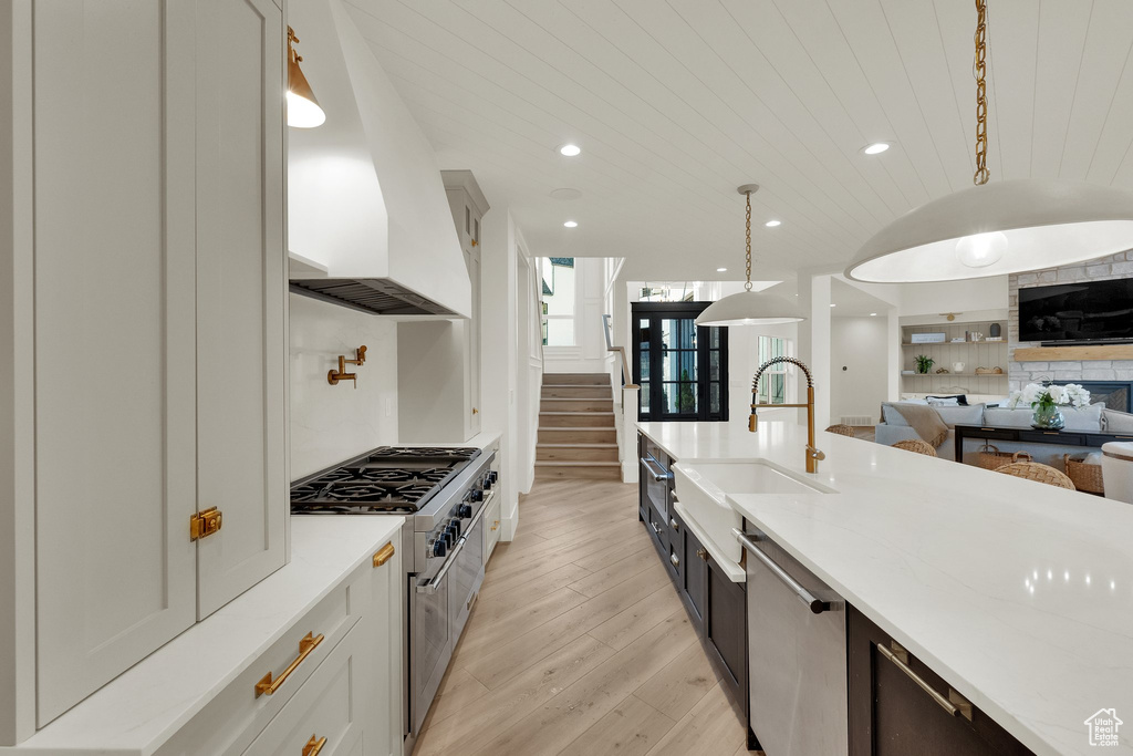 Kitchen featuring appliances with stainless steel finishes, light wood finished floors, custom range hood, decorative light fixtures, and open floor plan