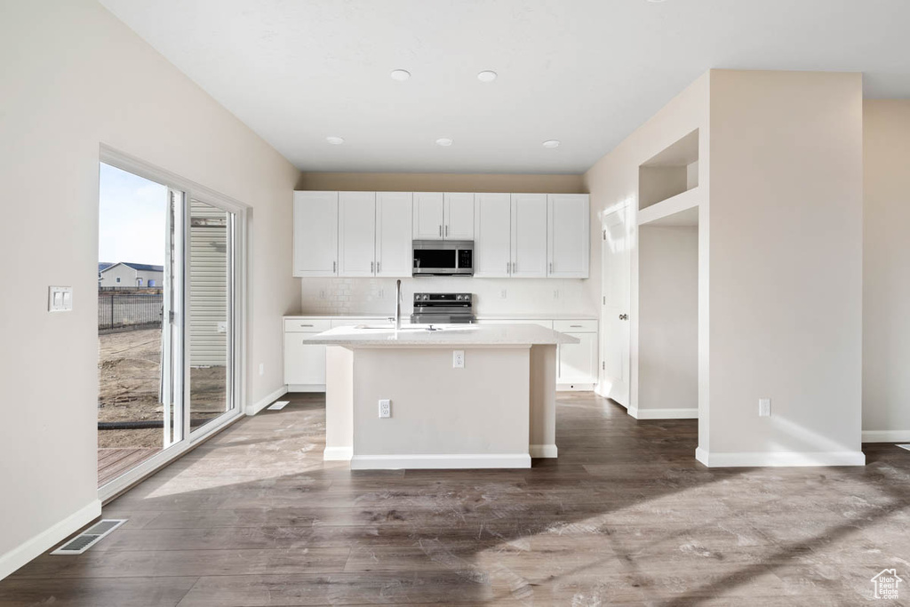 Kitchen with stainless steel microwave, stove, a center island with sink, white cabinets, and recessed lighting