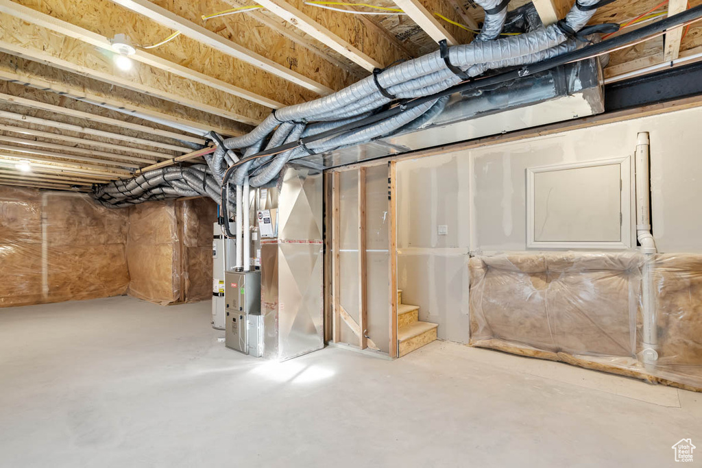 Unfinished below grade area featuring heating unit and strapped water heater