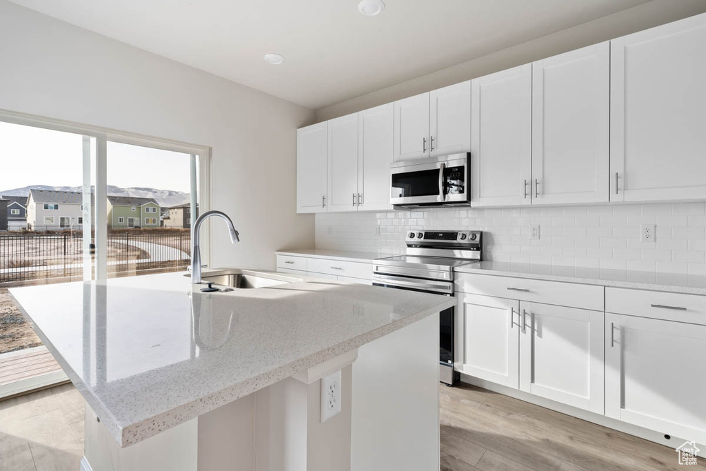 Kitchen with appliances with stainless steel finishes, light wood-style flooring, decorative backsplash, and white cabinets