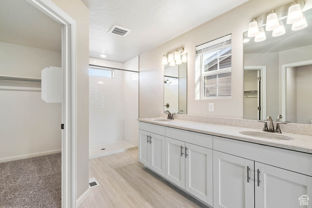 Bathroom with healthy amount of natural light, double vanity, tiled shower, and a spacious closet