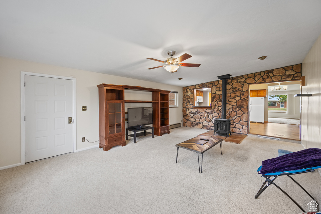 Carpeted living room with a wood stove, ceiling fan, and baseboard heating