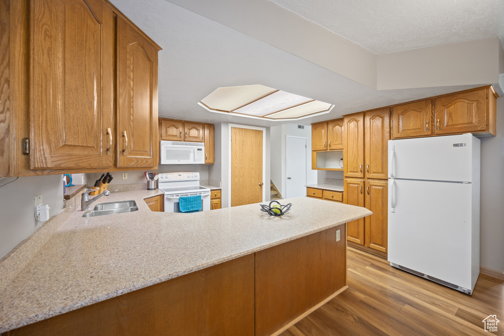 Kitchen featuring white appliances, light wood-type flooring, a peninsula, and brown cabinets