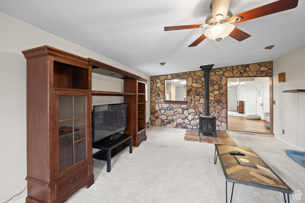 Living area featuring a wood stove, light colored carpet, and ceiling fan