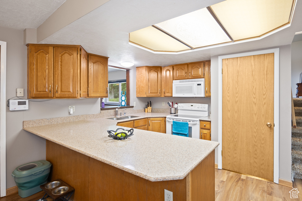 Kitchen with white appliances, a peninsula, light countertops, light wood-style flooring, and brown cabinetry