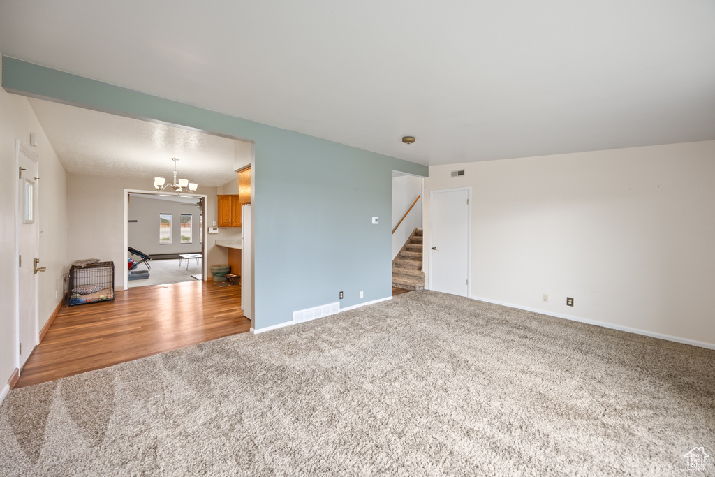 Unfurnished living room with carpet floors, stairway, a chandelier, and wood finished floors