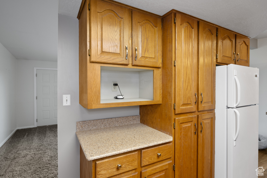 Kitchen with freestanding refrigerator, brown cabinets, and carpet floors