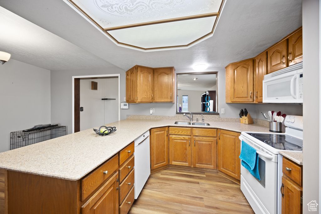 Kitchen featuring white appliances, light wood-type flooring, brown cabinetry, and a peninsula