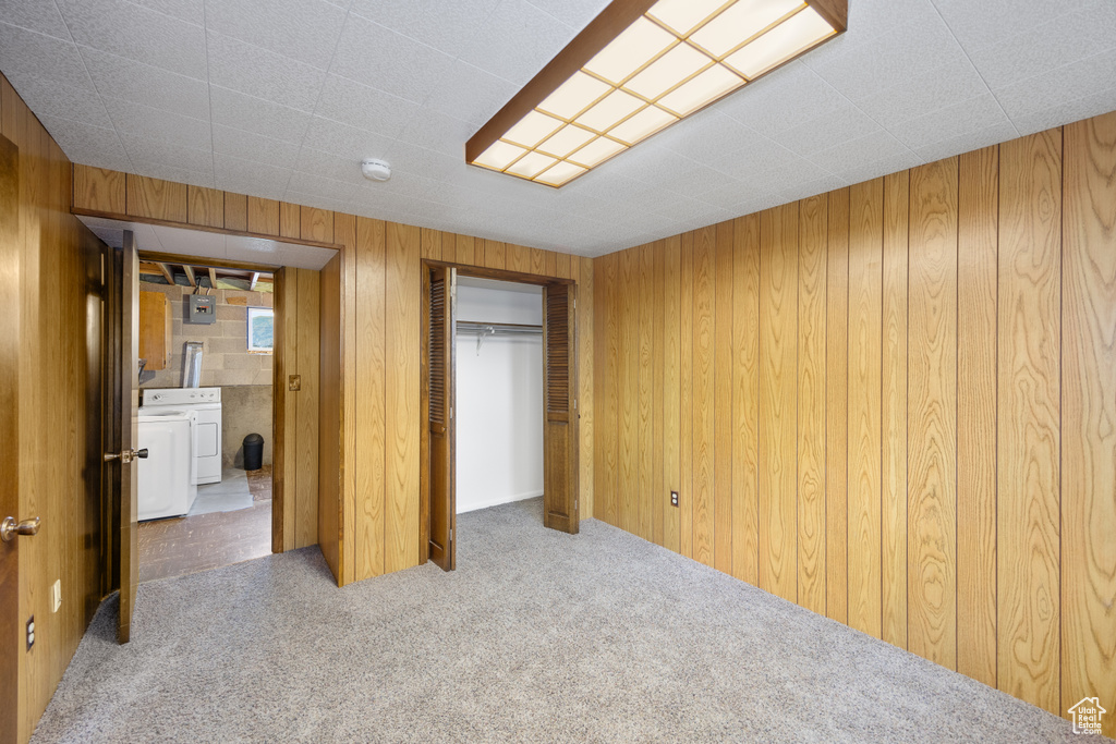 Unfurnished bedroom with carpet floors, wood walls, washer and clothes dryer, and a closet
