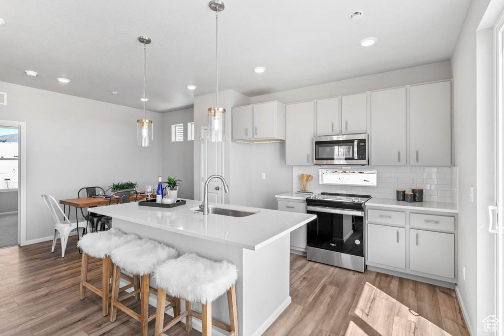 Kitchen with appliances with stainless steel finishes, light wood-style flooring, light countertops, tasteful backsplash, and pendant lighting