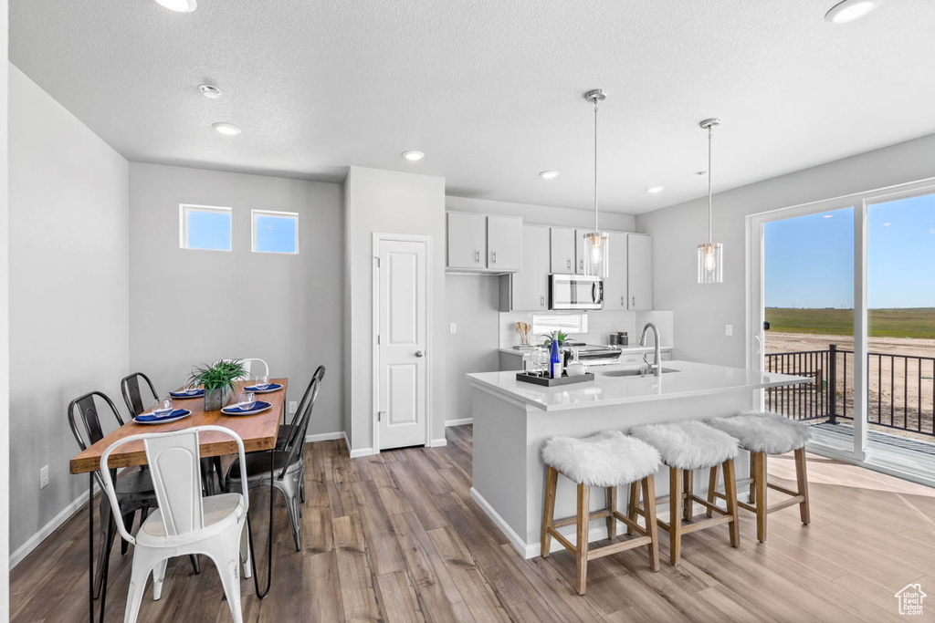 Kitchen with stainless steel microwave, a kitchen breakfast bar, light wood finished floors, white cabinets, and recessed lighting